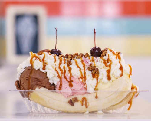 A banana split topped with chocolate, strawberry, and vanilla ice cream, whipped cream, nuts, and cherries.