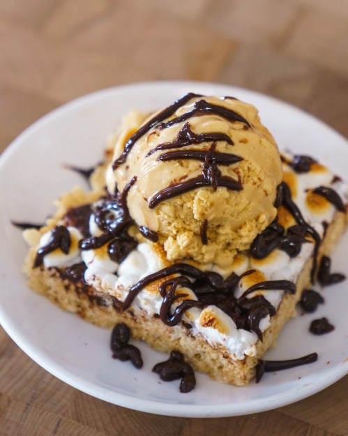 A slice of dessert topped with ice cream, drizzled with chocolate and caramel, on a white plate.