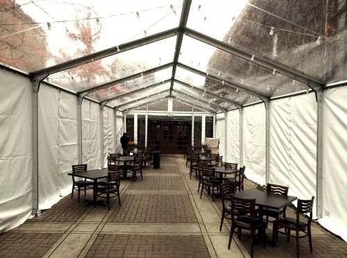 A spacious, empty tent with tables and chairs, featuring white walls and string lights, set in a courtyard.