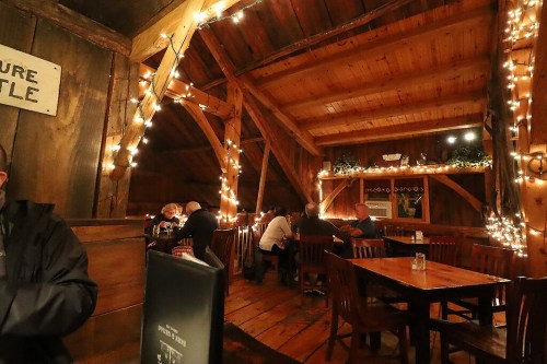 Cozy wooden interior of a restaurant, warmly lit with string lights, featuring diners at wooden tables.