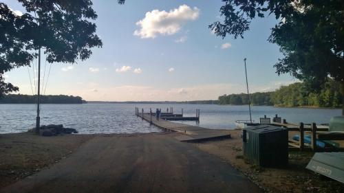 A serene lake view with a wooden dock, surrounded by trees and a clear sky, inviting for boating or relaxation.