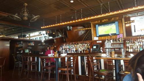 A cozy bar interior with wooden decor, a long counter, shelves of liquor, and a TV showing a sports game.