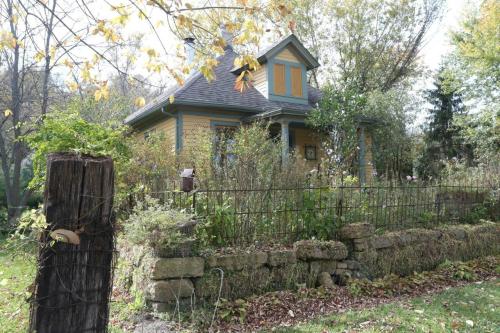 A charming yellow house surrounded by greenery and a stone wall, with autumn leaves scattered around.