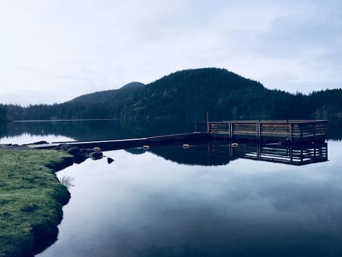 A serene lake scene with a wooden dock, surrounded by lush green hills and a calm, reflective water surface.