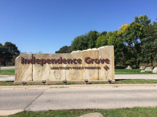 Sign for Independence Grove, a nature preserve in Lake County, surrounded by trees and a clear blue sky.