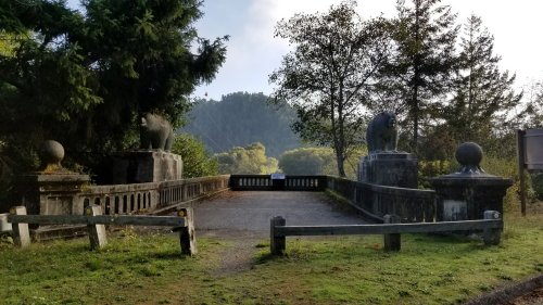 A stone bridge with lion statues on either side, surrounded by trees and greenery under a cloudy sky.