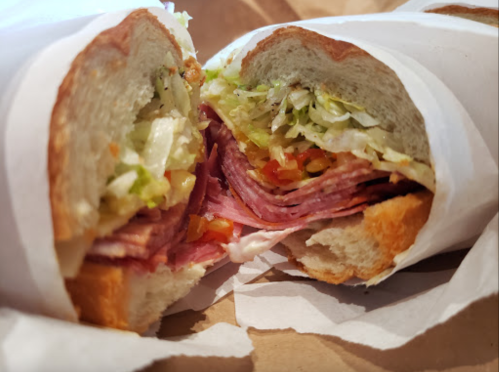 Close-up of a sandwich cut in half, featuring layers of deli meats, lettuce, and tomatoes in a toasted roll.