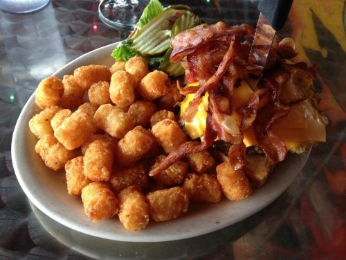 A plate of crispy tater tots alongside a cheeseburger topped with bacon and lettuce.