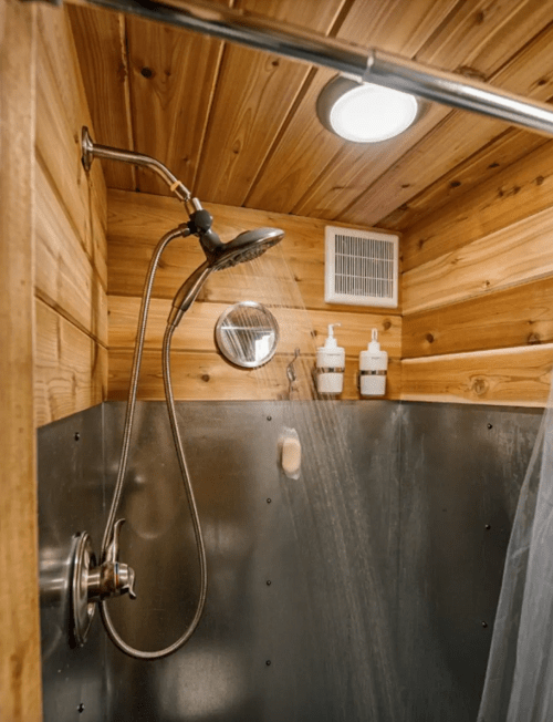 A wooden shower stall with a metal showerhead, water running, and two bottles on the wall.