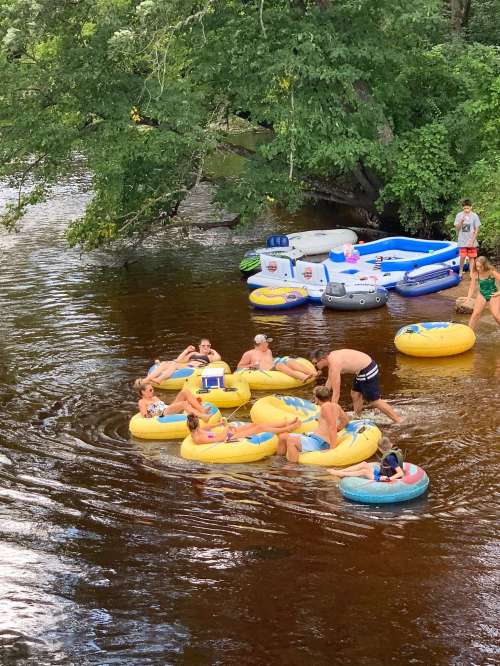 A group of people relax on yellow inner tubes in a river, surrounded by inflatable rafts and lush greenery.