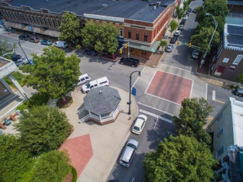 Aerial view of a town square with a gazebo, surrounding trees, and intersecting streets lined with buildings.