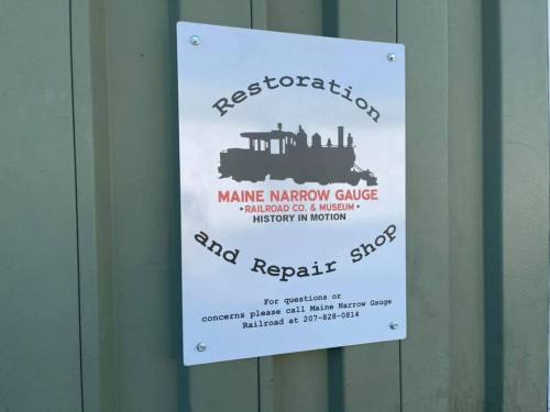 Sign for the Maine Narrow Gauge Railroad Restoration and Repair Shop, featuring a vintage train graphic.
