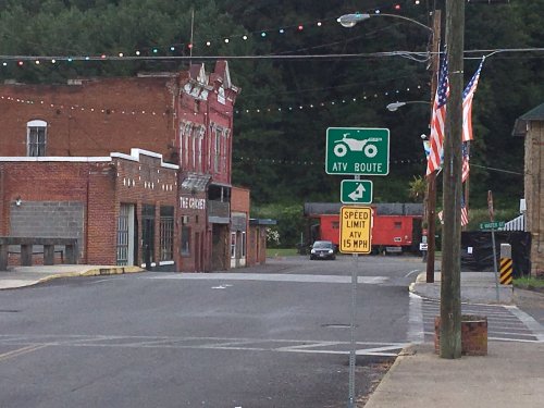 A quiet street in a small town with a tractor sign for ATV routes, flags, and historic buildings in the background.