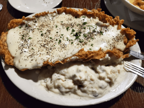 A plate of fried chicken topped with creamy gravy, served alongside a generous portion of mashed potatoes.