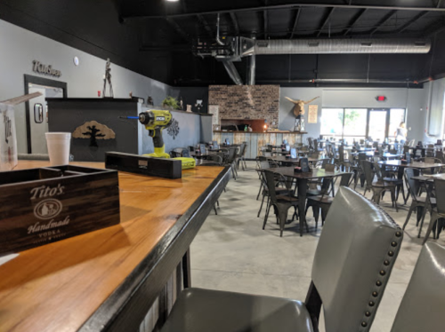 Interior of a restaurant with wooden tables, chairs, and a bar area, featuring a brick fireplace and tools on the counter.