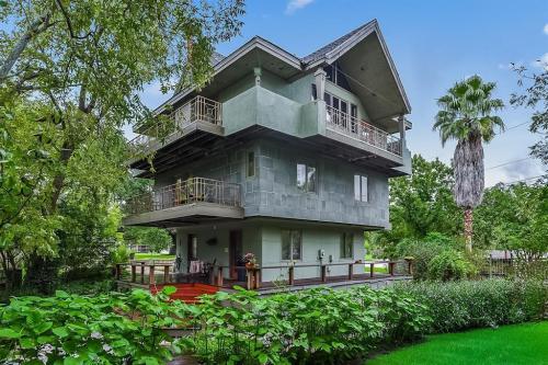 A modern three-story house surrounded by greenery, featuring multiple balconies and a unique architectural design.