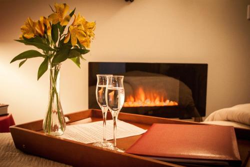 A cozy setting with a vase of flowers, two glasses of water, and a menu on a tray, with a glowing fireplace in the background.
