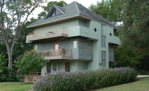 A modern three-story house with a unique design, surrounded by greenery and flowering plants.