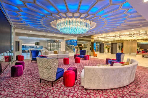 Modern lounge area featuring colorful seating, a large chandelier, and vibrant decor with a patterned carpet.