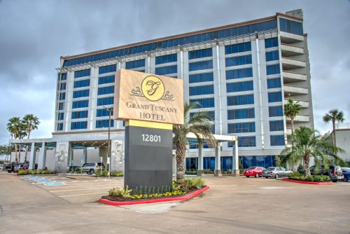 Exterior view of the Grand Tuscany Hotel, featuring a large sign and modern architecture with palm trees in the foreground.