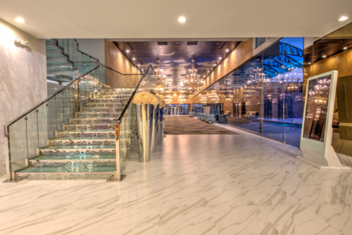Elegant lobby with a glass staircase, decorative chandeliers, and large windows reflecting a modern design.
