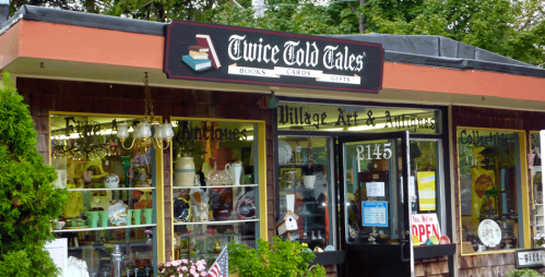 Exterior of "Twice Told Tales" shop featuring books, cards, and gifts, with a welcoming open sign.