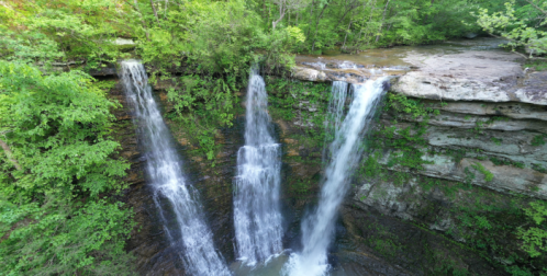 A scenic view of three waterfalls cascading down rocky cliffs, surrounded by lush green trees and foliage.