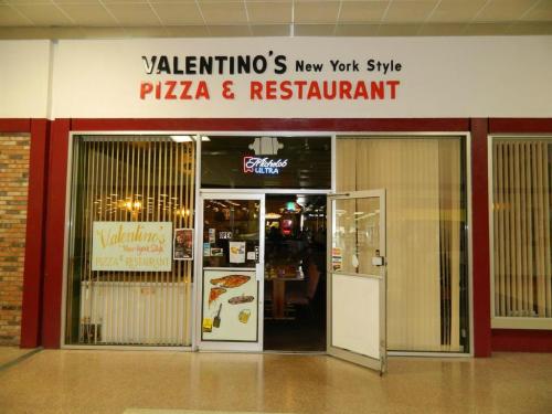 Valentino's New York Style Pizza & Restaurant entrance with large sign and glass doors, featuring a menu display.