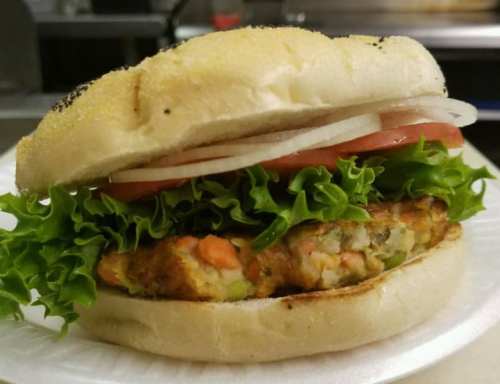 A close-up of a sandwich with a veggie patty, lettuce, tomato, and onion, served in a toasted bun.
