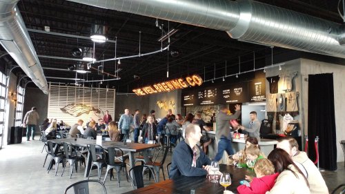 A bustling brewery interior with patrons enjoying drinks, a bar area, and a large "Brewing Co" sign on the wall.