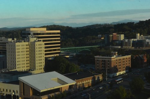 A cityscape featuring buildings, a bridge, and mountains in the background under a clear sky.