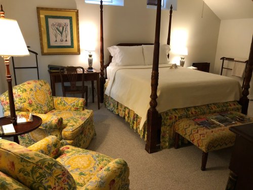 Cozy bedroom featuring a four-poster bed, floral armchairs, and warm lighting, creating a welcoming atmosphere.