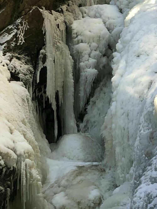 A frozen waterfall with icicles and snow-covered rocks, creating a serene winter landscape.