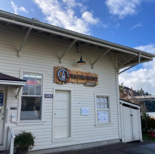 Exterior of the Waterfront Depot building, featuring a wooden sign and an "Open" neon light. Clear blue sky above.