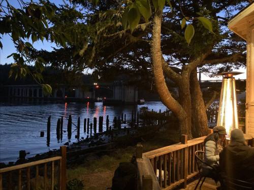 A serene riverside scene at dusk, featuring a tree, water reflections, and a cozy outdoor seating area.