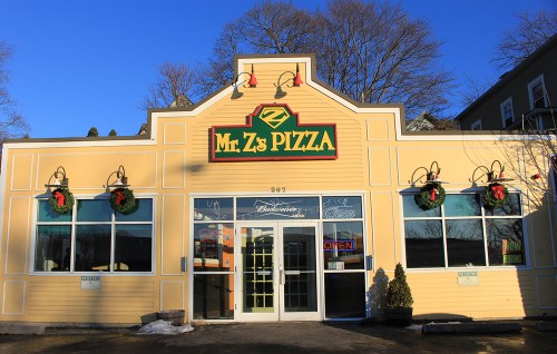 Exterior of Mr. Z's Pizza, a yellow building with festive wreaths, large windows, and an "OPEN" sign.