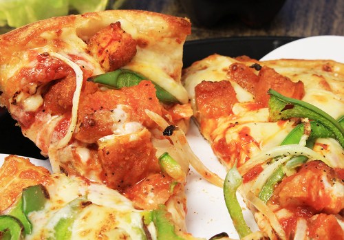 Close-up of pizza slices topped with cheese, green peppers, and chunks of chicken on a white plate.