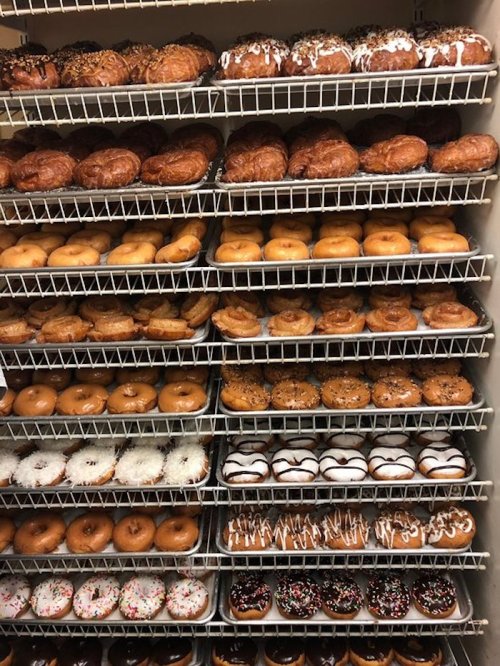 A display of various donuts on wire racks, featuring glazed, frosted, and sprinkled varieties.