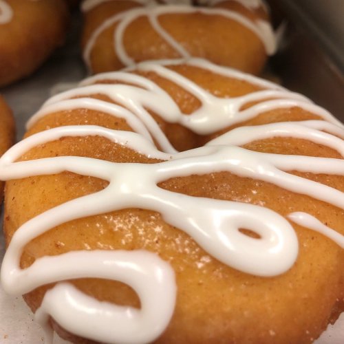 Close-up of a glazed donut with white icing drizzled in a decorative pattern on top.