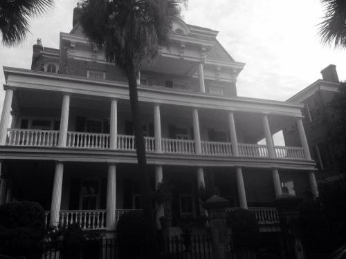 A large historic house with a grand porch, palm trees, and a cloudy sky in black and white.