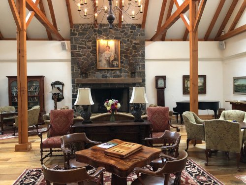 Cozy lounge with wooden beams, a stone fireplace, vintage furniture, and a chandelier, creating a warm atmosphere.