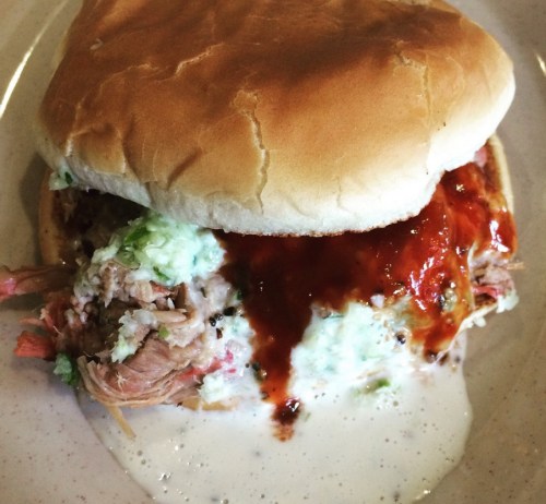 A close-up of a pulled pork sandwich with lettuce, sauce, and a soft bun on a plate.