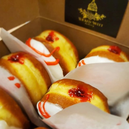 A box of freshly baked donuts filled with cream and topped with red fruit jam.