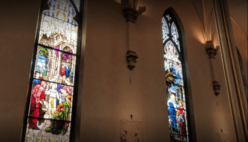 Stained glass windows depicting biblical scenes in a church interior, with intricate designs and vibrant colors.