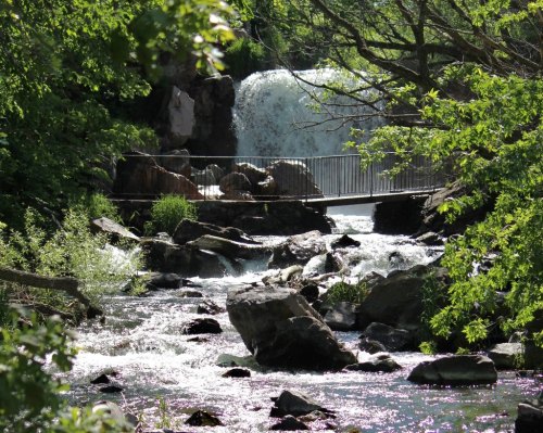A serene landscape featuring a waterfall cascading over rocks, surrounded by lush greenery and a flowing stream.