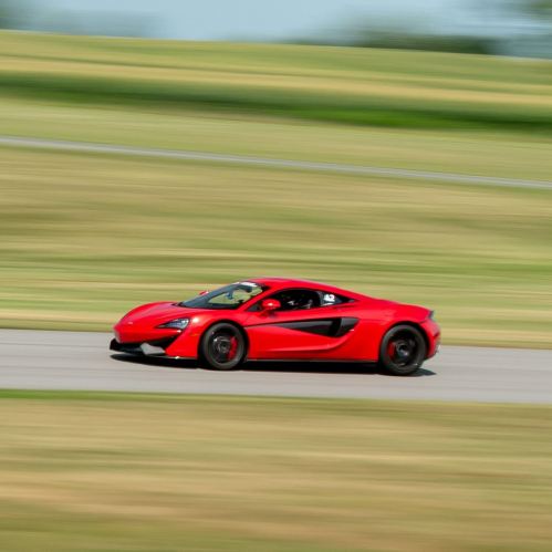 A red sports car speeds along a racetrack, with blurred green fields in the background.
