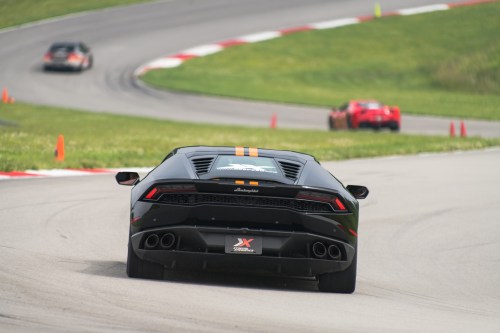 A black Lamborghini Huracán speeds around a racetrack, with colorful cones marking the course in the background.