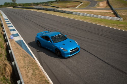 A blue sports car speeds around a racetrack, with curves and grassy areas in the background.