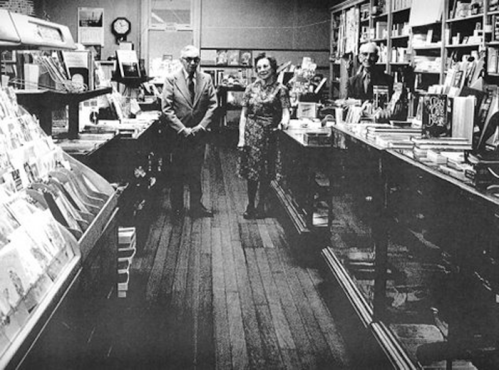 Three people stand in a vintage bookstore, surrounded by shelves of books and a warm, inviting atmosphere.