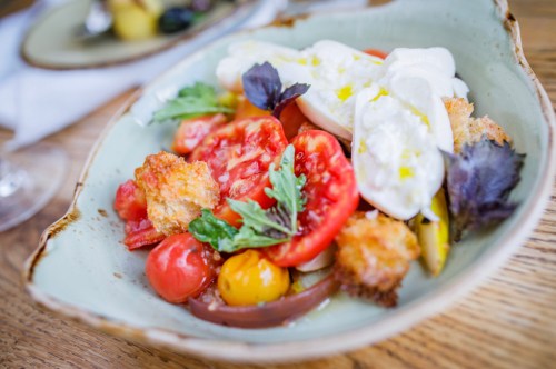 A colorful salad with fresh tomatoes, greens, croutons, and creamy burrata served in a rustic bowl.